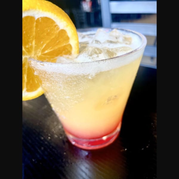 A vibrant, layered cocktail with ice and an orange slice, served at Firehouse Pizza.