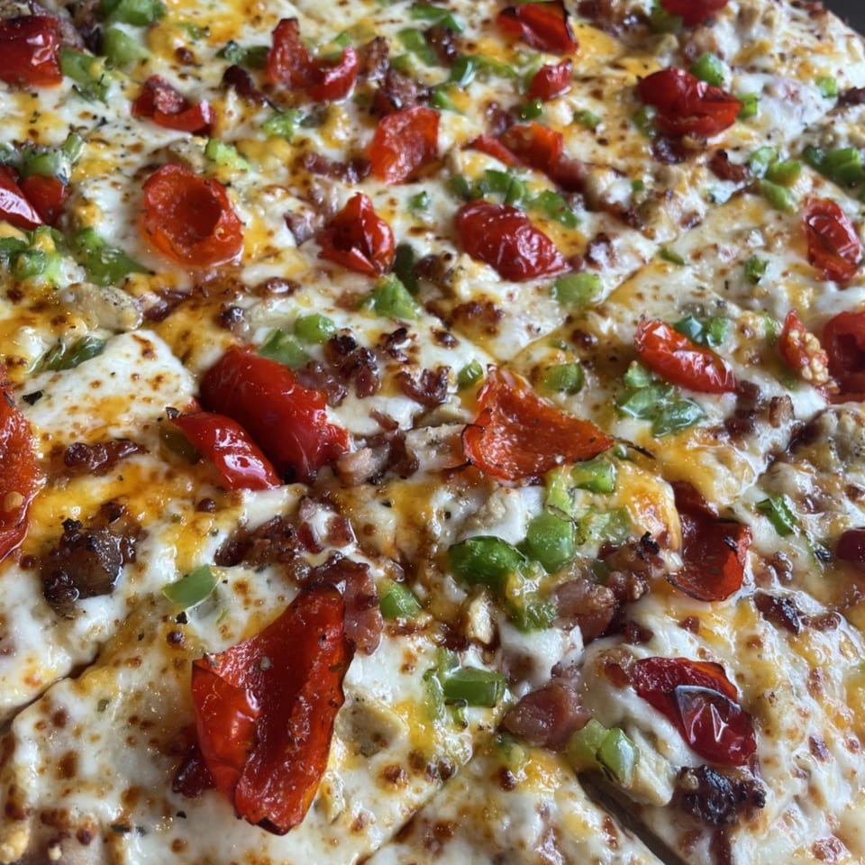 Close-up of a Firehouse Pizza with melted cheese, red peppers, green peppers, and sausage.
