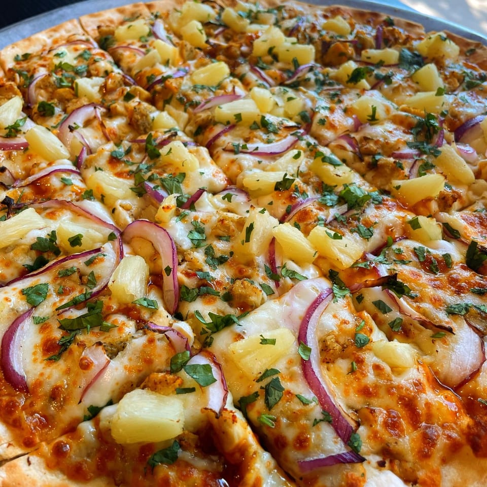 Close-up of a Firehouse Pizza with pineapple, red onion, chicken, and cilantro.