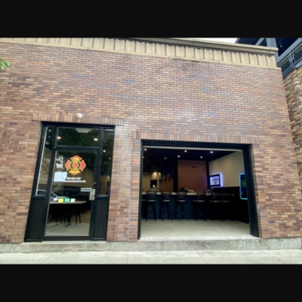 Exterior of Firehouse Pizza, a brick building with a glass entrance and an open garage-style door revealing a bar.
