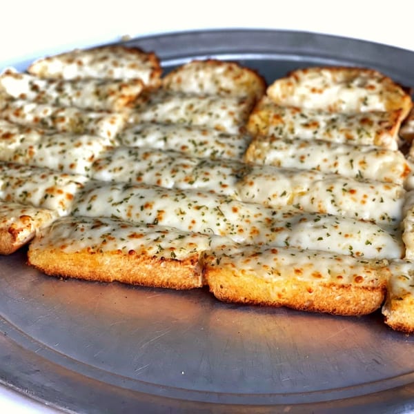 Cheesy breadsticks with herbs on a metal pizza pan, ready to be served at Firehouse Pizza.