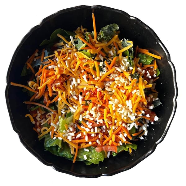 A black bowl filled with a salad topped with shredded orange and white cheese.