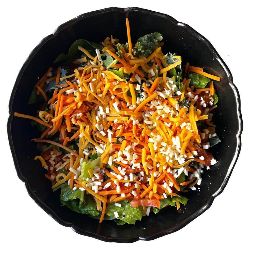 A black bowl filled with a salad topped with shredded orange and white cheese.