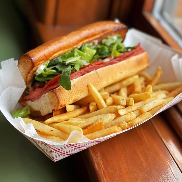 A Firehouse Pizza sub sandwich with lettuce and meat, served with a side of golden french fries.