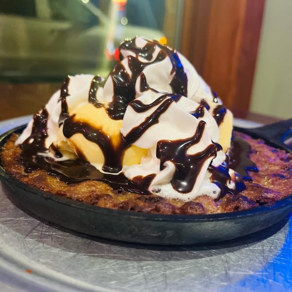 Warm chocolate chip cookie skillet topped with vanilla ice cream, whipped cream, and chocolate syrup.